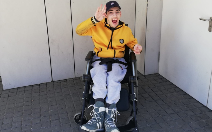 Chłopiec w wózku inwalidzkim, uśmiechający się i machający.
