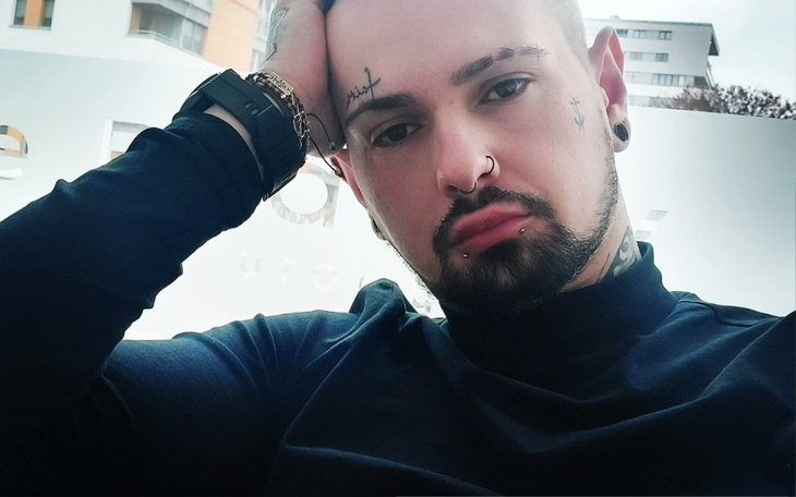 Mężczyzna z tatuażami, siedzący z zamyśloną miną.