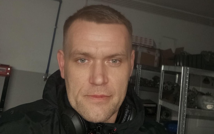 Mężczyzna w ciemnej kurtce, z słuchawkami na szyi, w pomieszczeniu.