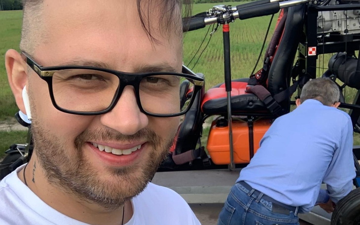 Mężczyzna w okularach, uśmiechający się przy helikopterze.