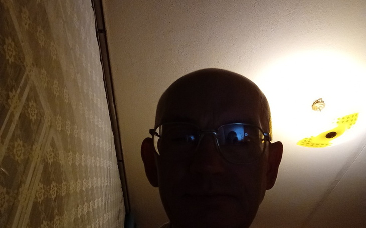 Mężczyzna z okularami w słabym oświetleniu, z lampą w tle.