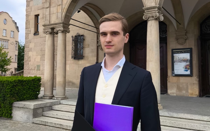 Młody mężczyzna w eleganckim stroju przed budynkiem.