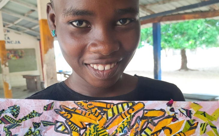 Chłopiec trzymający kolorowy rysunek z uśmiechem.