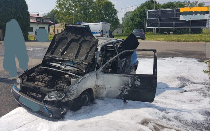 Spalony samochód na drodze, otoczony przez pianę gaśniczą.