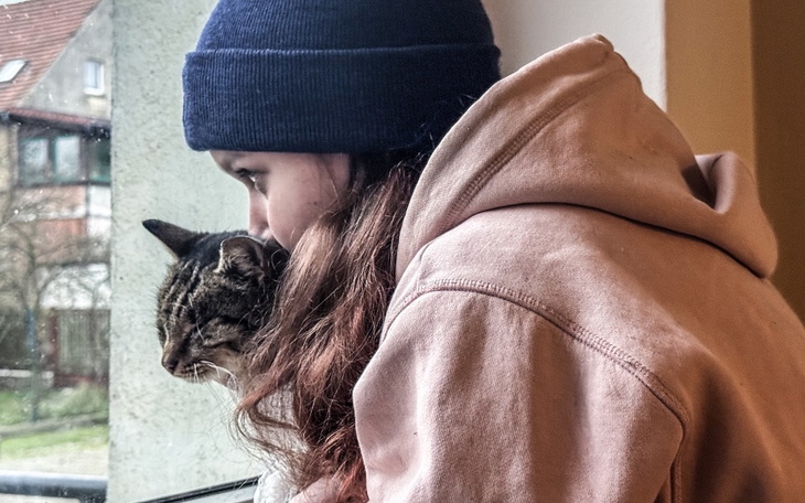 Dziewczyna w czapce przytulająca kota, patrząca przez okno.