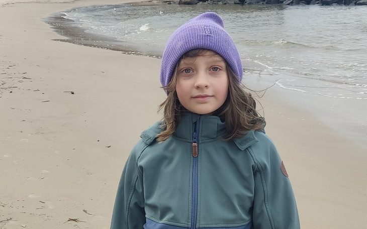 Dziecko na plaży, w ciepłej kurtce i czapce.