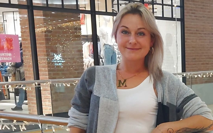 Kobieta w szarej bluzie, uśmiechająca się w centrum handlowym.