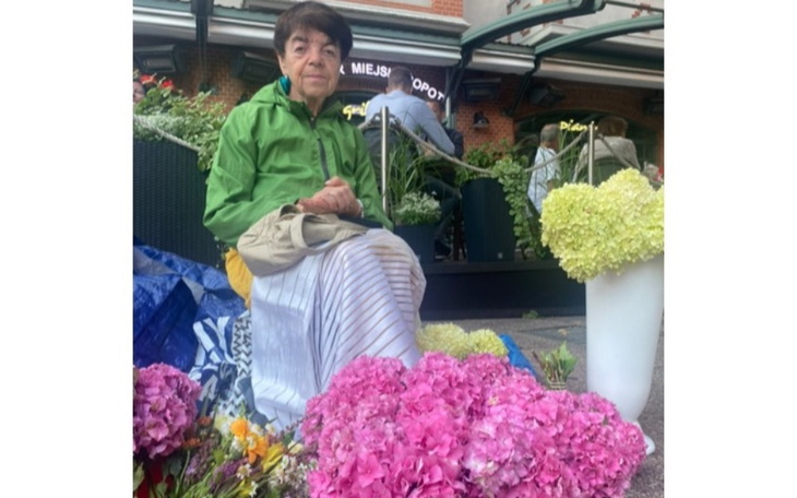 Osoba sprzedająca kwiaty na ulicy, otoczona kolorowymi bukietami.