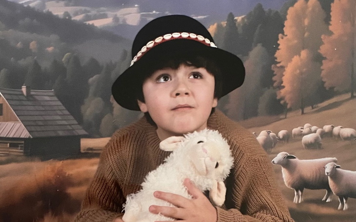 Chłopiec w kapeluszu trzymający pluszowego baranka na tle gór.