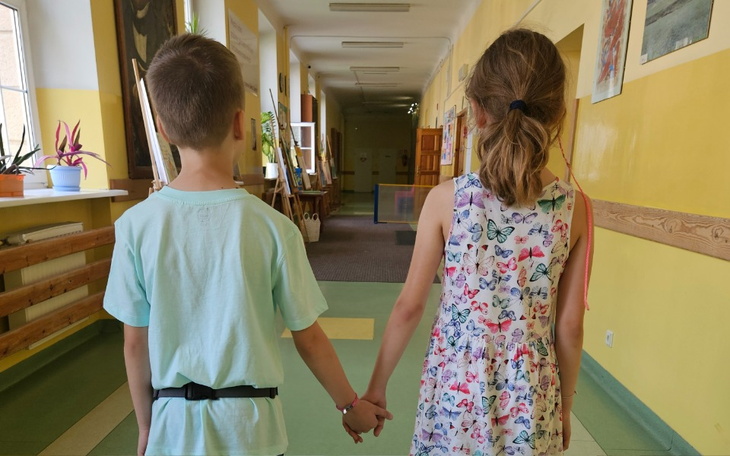 Dwoje dzieci trzymających się za ręce w szkolnym korytarzu.