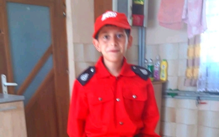 Chłopiec w czerwonym mundurze, uśmiechający się do kamery.