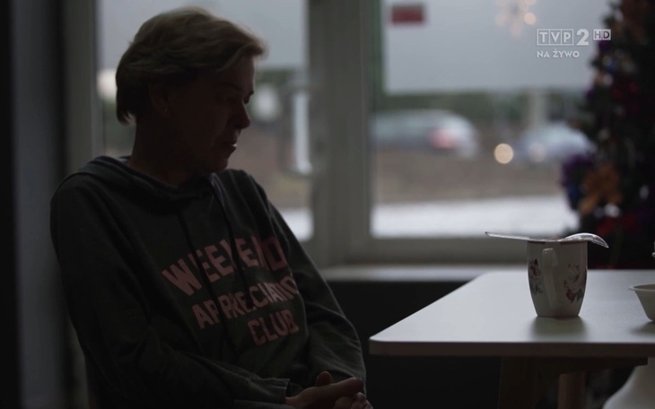 Osoba siedzi przy stole, w tle widoczny kubek.