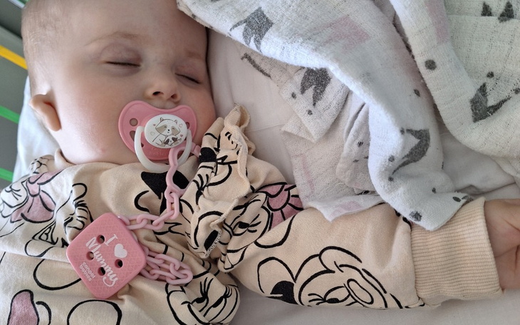 Śpiące dziecko z smoczkiem w różowym ubranku.