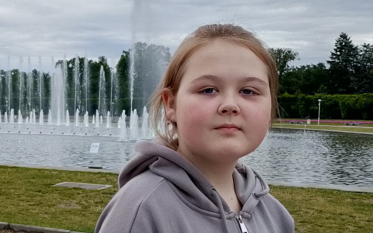 Dziewczynka przy fontannie, z poważnym wyrazem twarzy.