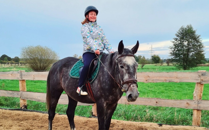 Dziewczynka na koniu, uśmiechająca się do kamery.