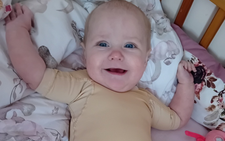 Uśmiechnięte niemowlę leżące na łóżku w otoczeniu poduszek.