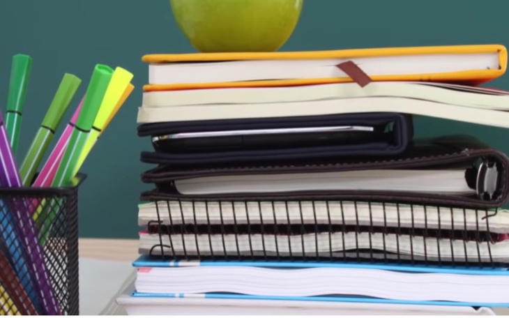 Stos zeszytów i przyborów szkolnych na biurku.