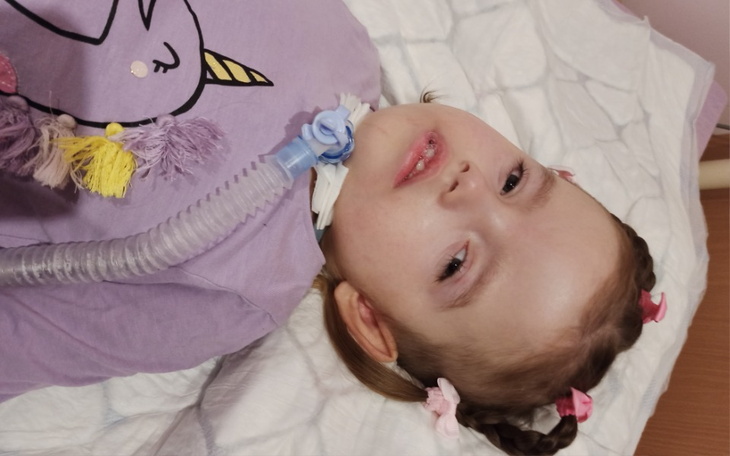 Dziewczynka leży na łóżku, uśmiechając się, z rurką do oddychania.