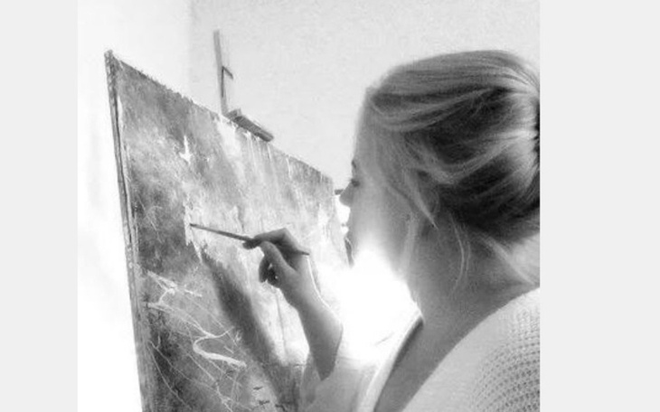 Kobieta malująca obraz, trzymająca pędzel w dłoni.