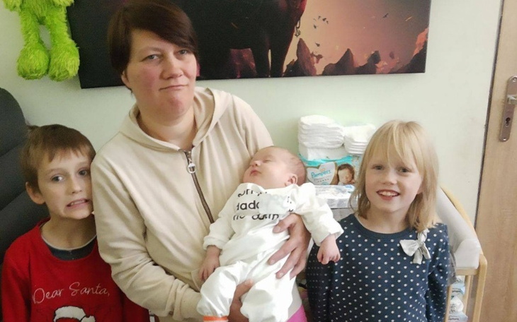 Rodzina z noworodkiem, uśmiechająca się do kamery.