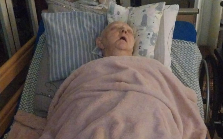 Starsza osoba leżąca w łóżku, przykryta kocem.