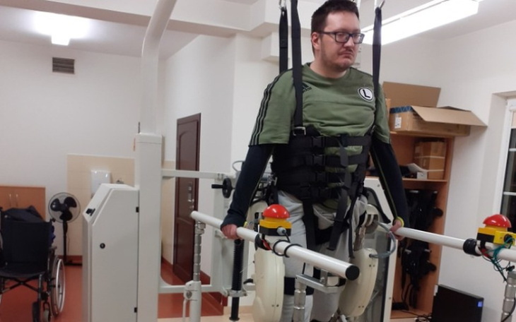 Mężczyzna w specjalnym urządzeniu rehabilitacyjnym, skupiony.
