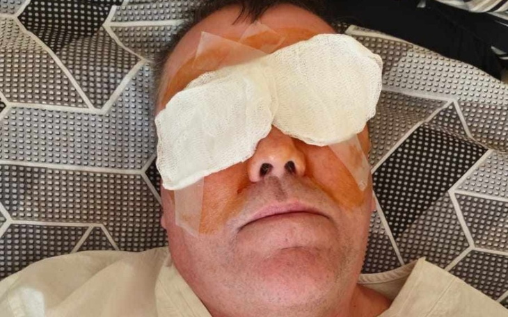 Mężczyzna z opatrunkami na oczach, leżący na łóżku.