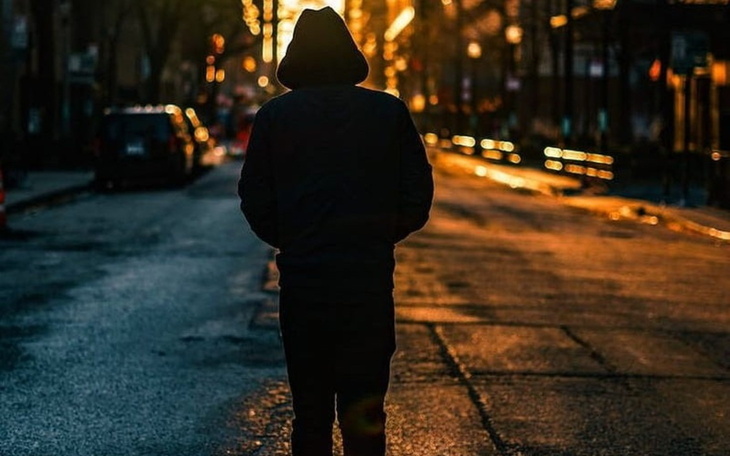 Postać w kapturze spacerująca po ulicy o zachodzie słońca.