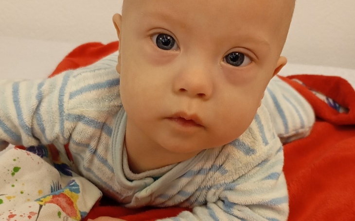 Mały chłopiec w piżamie, leżący na czerwonym kocyku, z ciekawym spojrzeniem.