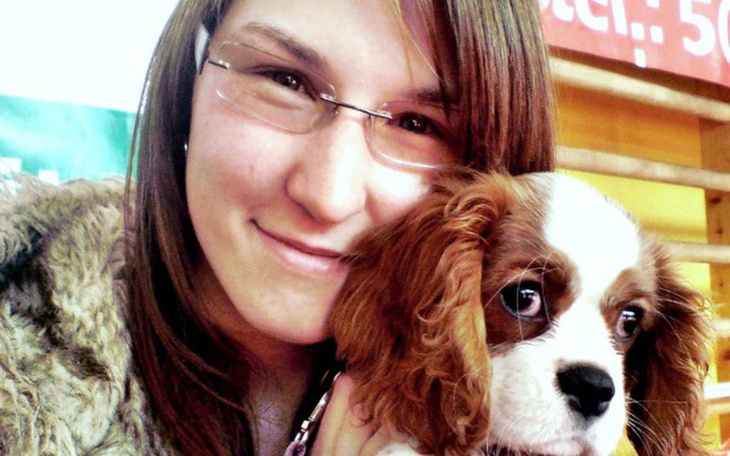 Młoda kobieta z psem na rękach, oboje uśmiechnięci.