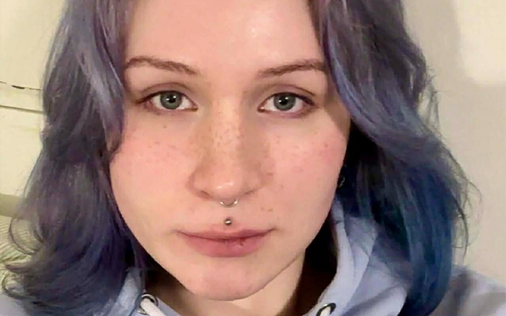 Portret młodej kobiety z niebieskimi włosami i kolczykiem w nosie.