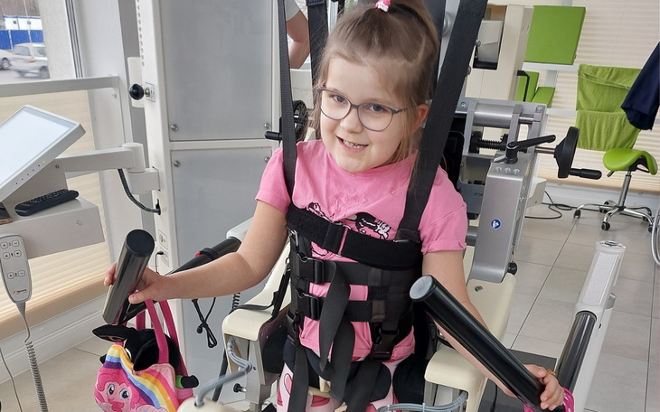 Dziewczynka w sprzęcie rehabilitacyjnym, uśmiechająca się.