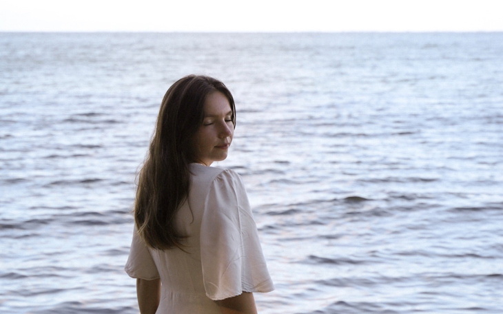 Kobieta w białej sukience stoi nad wodą, patrząc w dal.