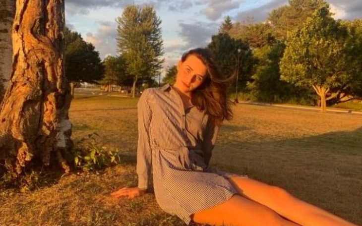 Kobieta w letniej sukience siedząca na trawie w promieniach słońca.