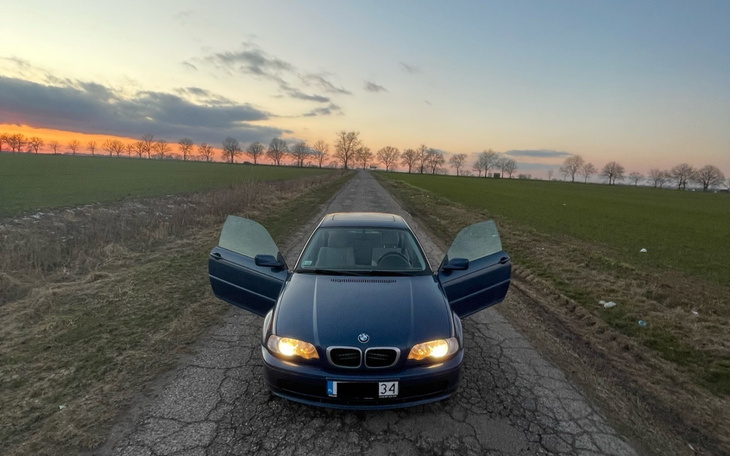 Samochód na drodze, drzwi otwarte, w tle zachód słońca.