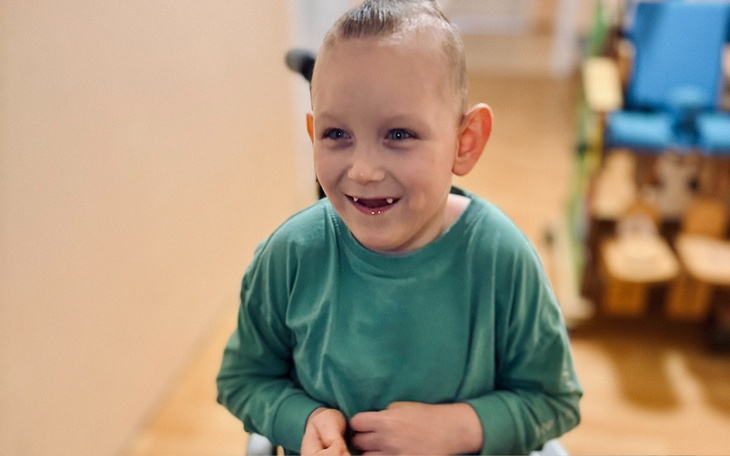 Chłopiec w wózku uśmiecha się do kamery.