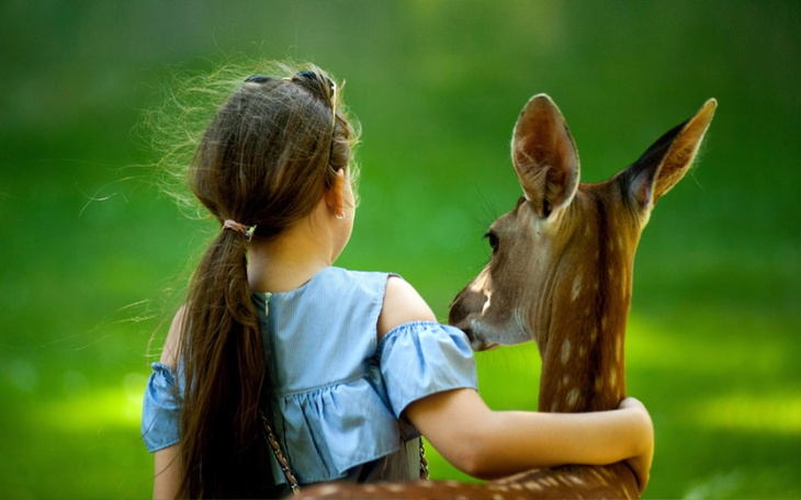 Dziewczynka obejmująca jelenia w zielonym otoczeniu.