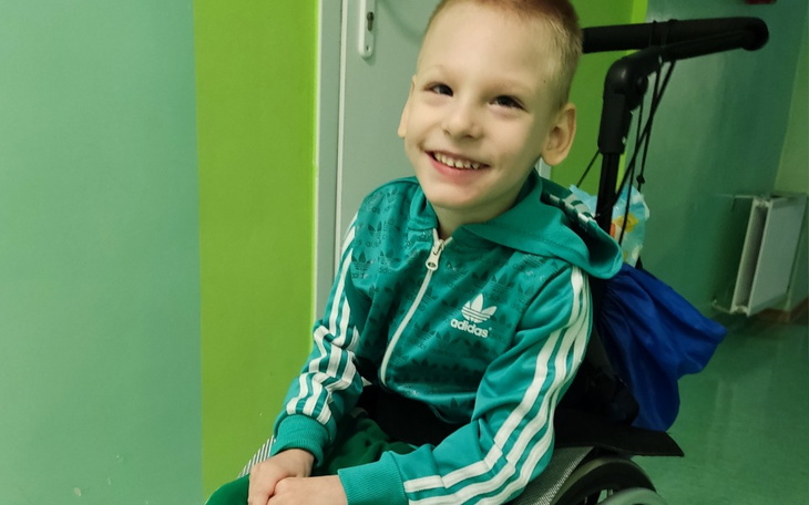 Uśmiechnięty chłopiec w wózku inwalidzkim, ubrany w zielony dres.