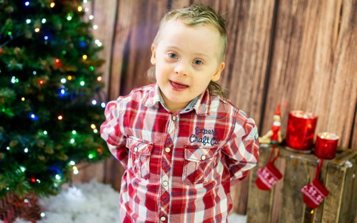 Chłopiec w koszuli w kratę, pozujący przy choince.