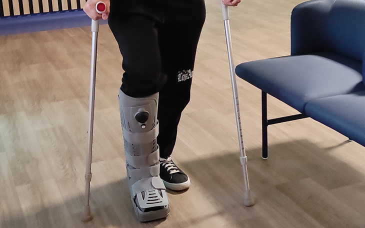 Osoba w specjalnym bucie ortopedycznym, używająca kul.