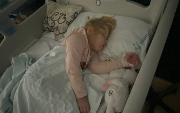 Mała dziewczynka śpiąca w łóżku szpitalnym, przytulająca pluszowego królika.