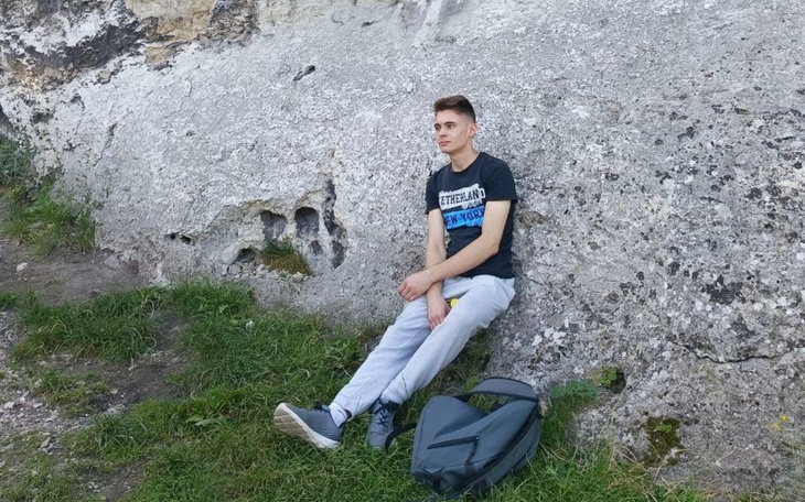 Młody mężczyzna siedzący na tle skalnej ściany.