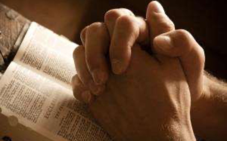 Złożone dłonie modlące się nad otwartą książką.