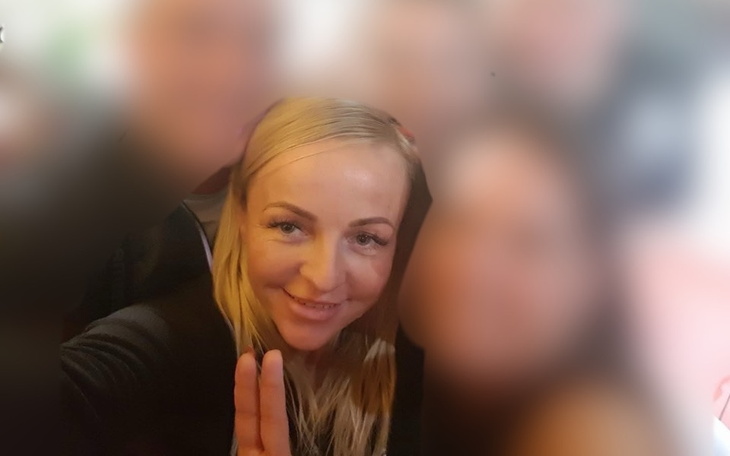 Rozmyta fotografia kobiety z uśmiechem, w tle inne osoby.