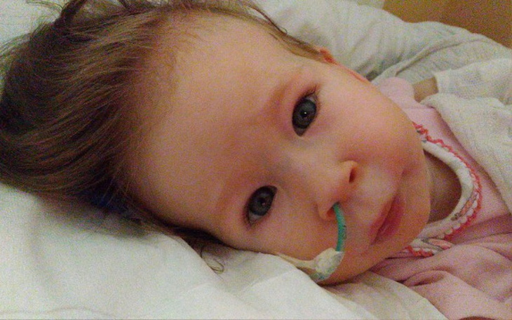 Mała dziewczynka leży na poduszce, z rurką tlenową w nosie, z wyrazem ciekawości.