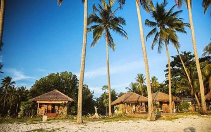 Tropikalna plaża z palmami i domkami w tle.