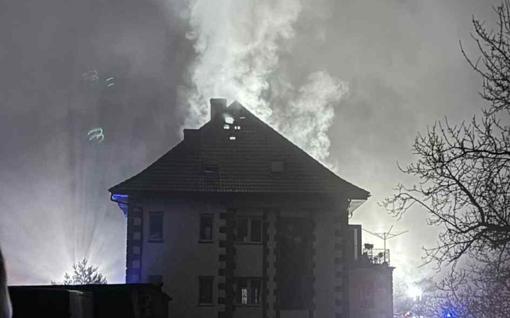 Zniszczony budynek po pożarze, dym unoszący się w nocy.