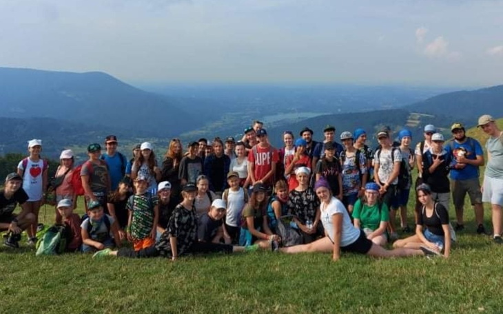 Grupa młodzieży na szczycie góry, w tle piękny widok.