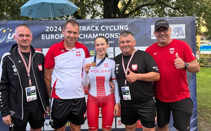 Zespół kolarzy z medalistką na tle banneru mistrzostw.