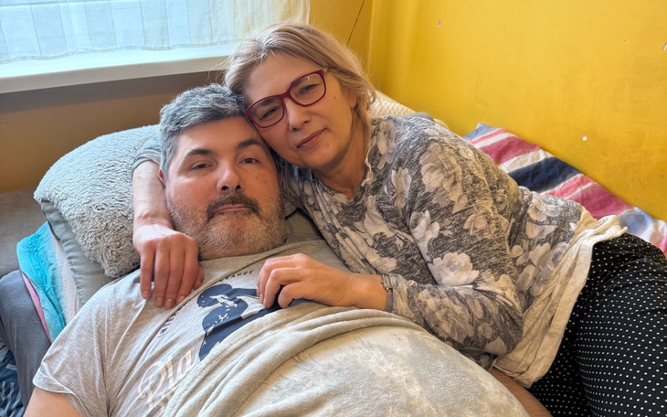 Para przytulająca się na łóżku, w tle żółta ściana.